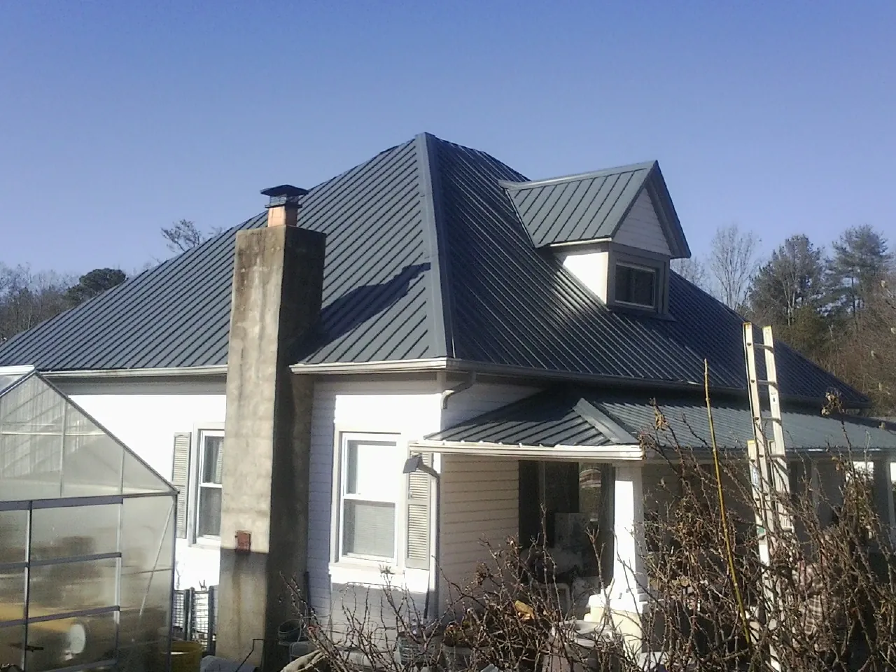 Dark blue standing seam metal roof on a white farmhouse with dormer — Slate & Tile Roof Repair by Roofing Brothers in Yanceyville