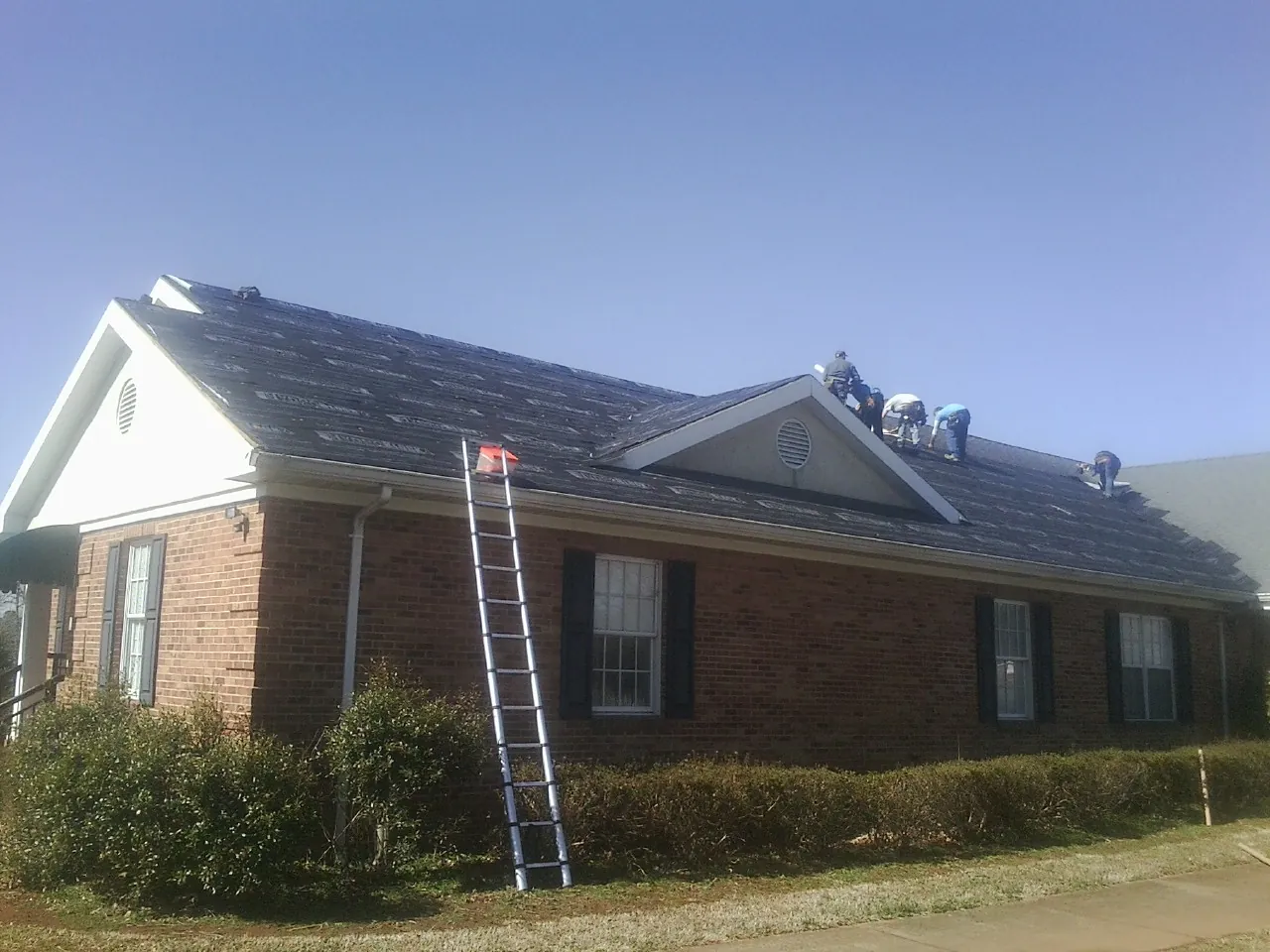 Crew tearing shingles off a brick ranch roof with a ladder set — Metal Roof Repair work by our crew in Yanceyville