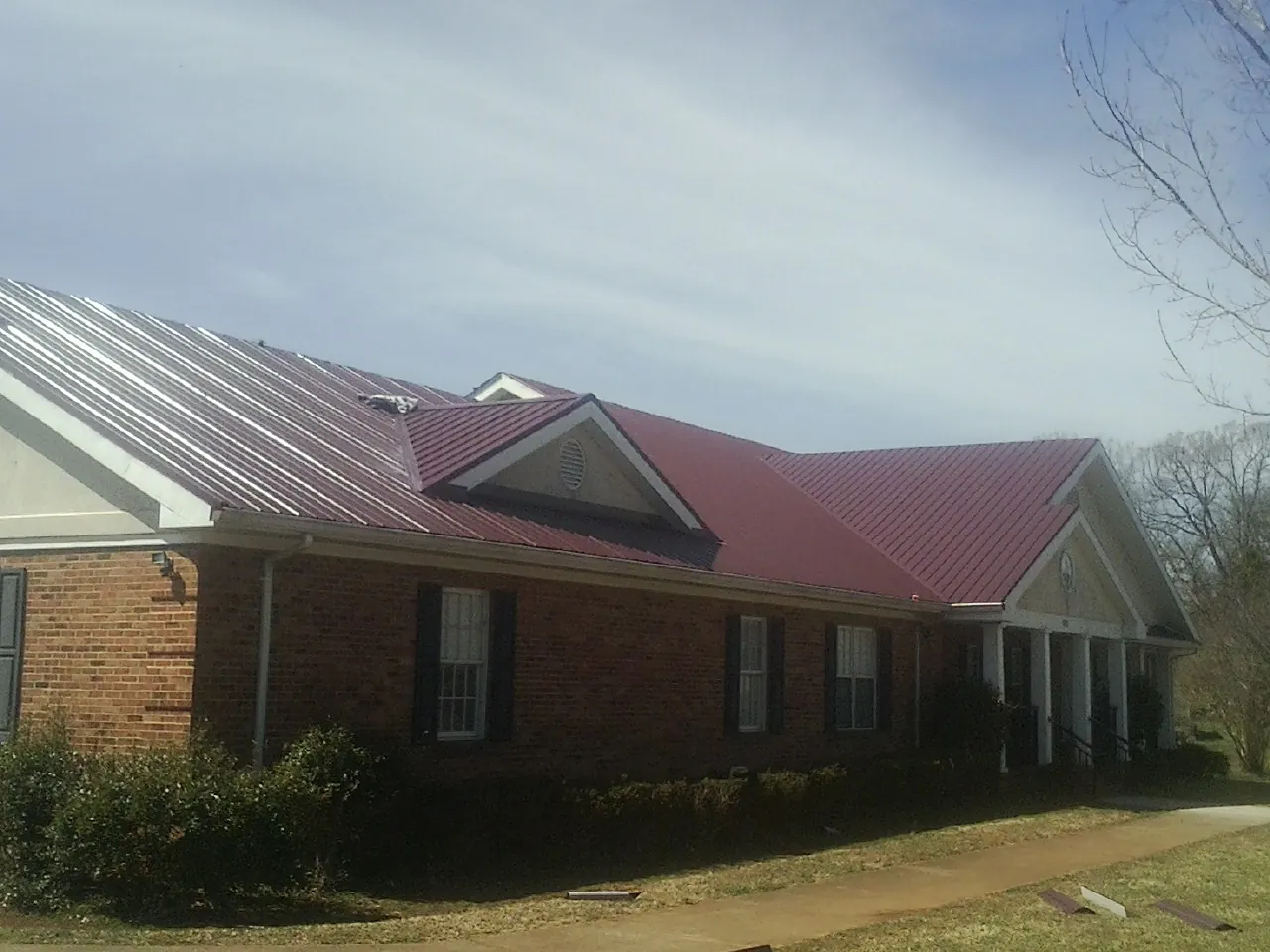 Red metal roof with gabled entries on a long brick building, from a Hail Damage Roof Repair job in Yanceyville