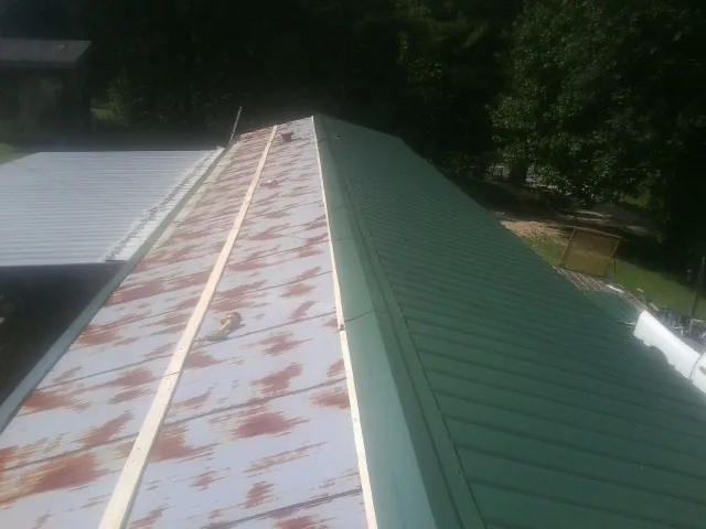 Old rusted panels beside newly installed green metal roofing — Wind Damage Roof Repair by Roofing Brothers in Yanceyville