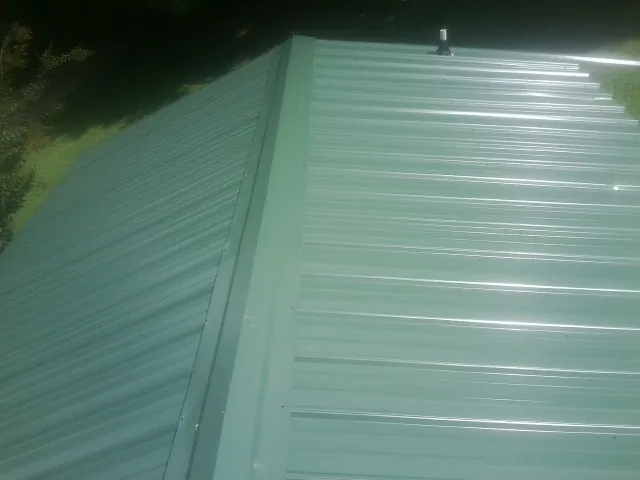 New green metal panels meeting at the ridge of a roof — Flat Roof Repair work by our crew in Yanceyville