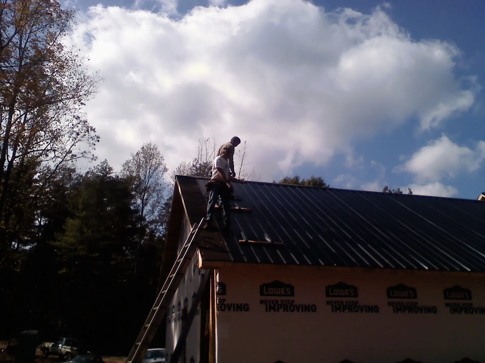 Roofer fastening dark metal panels high against a cloudy sky, from a Roof Inspection job in Yanceyville