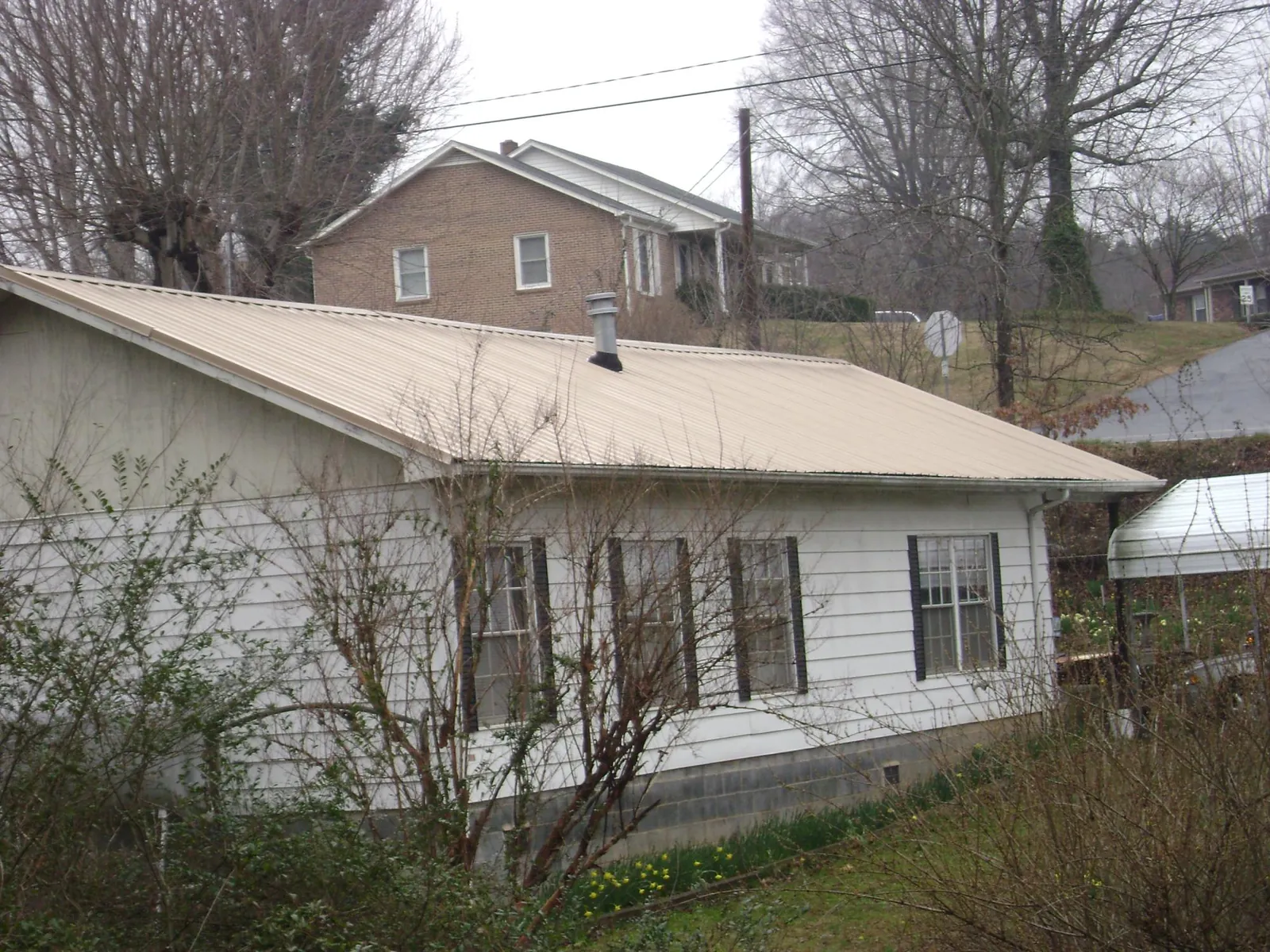 Tan metal roof on a white sided house set into a hillside — Commercial Roofing by Roofing Brothers in Yanceyville