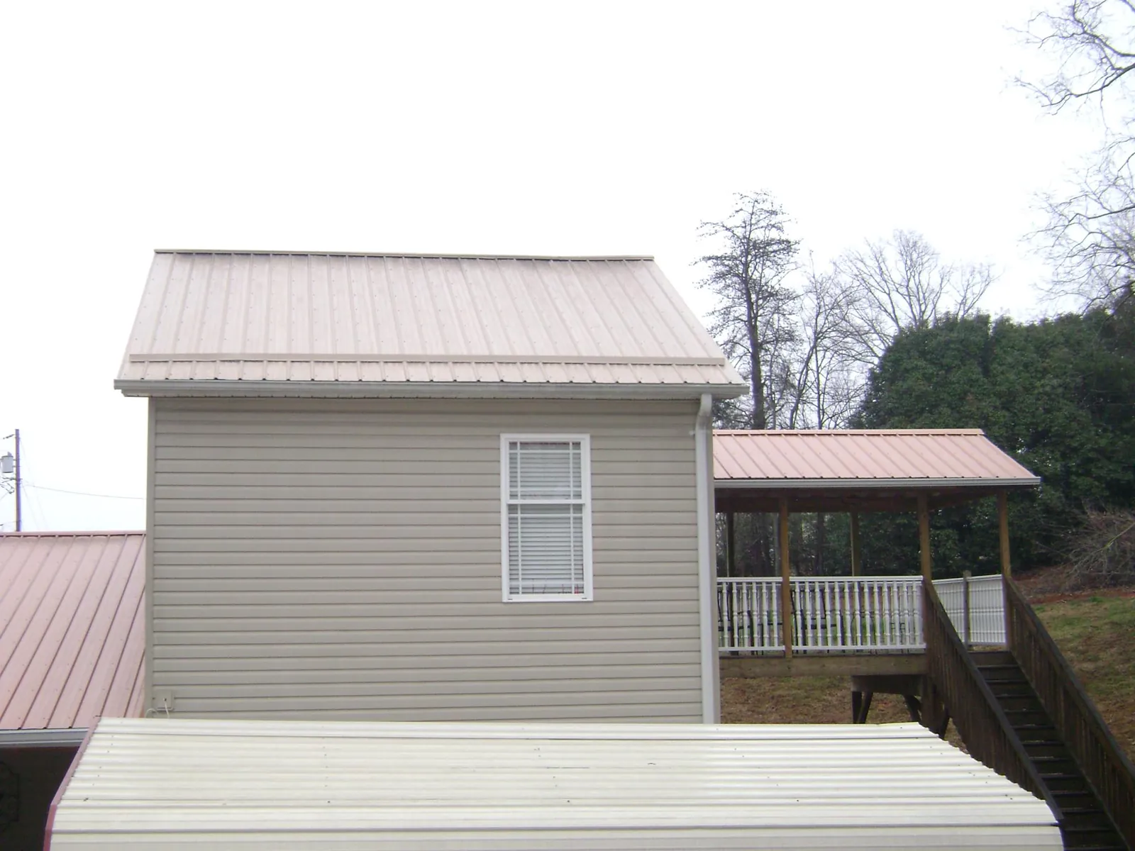 Tan metal roofs on a two story addition and attached porch, from a Roof Replacement job in Yanceyville